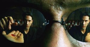 A close-up shot from The Matrix showing the reflection in Morpheus' sunglasses. In one lens, Neo (Keanu Reeves) is reaching for a red pill from Morpheus’ outstretched hand, while in the other lens, Neo is seen contemplating the choice. The scene symbolizes Neo's pivotal decision between the red pill (truth) and the blue pill (illusion).